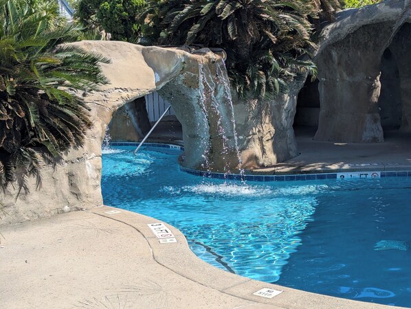 A pool with clear blue water, surrounded by palm trees and rocky formations.