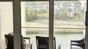 A room with three wicker chairs facing a window overlooking a pond and a wooden bridge. - Resort access & golf cart included. On tidal creek. Easy walk to beach. Reviews+ (Fripp Island)