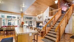 A spacious living area with a wooden staircase, a fireplace, and a large island with seating.