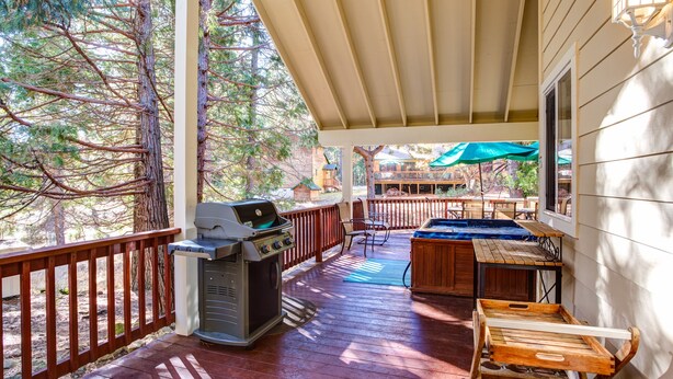 A covered outdoor deck with a grill, a hot tub, and wooden furniture.