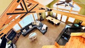 En rummelig, loft-agtig opholdsstue med højt til loftet, synlige træbjælker, en sort lædersofa, et spisebord og et køkkenområde med en sort bordplade.