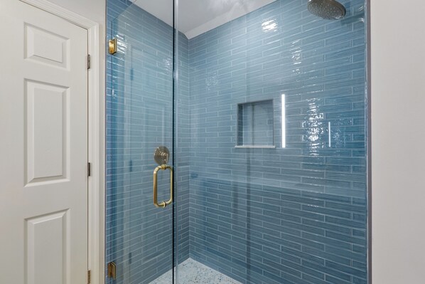 Eine gläserne Dusche mit blau gefliesten Wänden, einem goldenen Türgriff und einem kleinen Fenster.