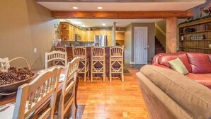 Una sala de estar acogedora con una mesa de comedor de madera y sillas, un sofá de cuero rojo, y una cocina al fondo.