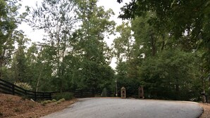 A paved road curving through a wooded area with a stone structure and a wooden fence.