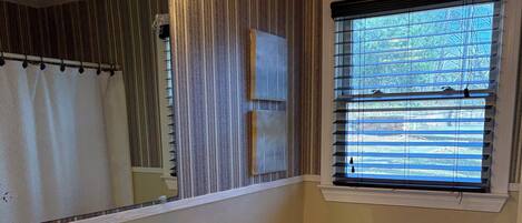 A bathroom with a white sink, toilet, and vanity. There is a window with blinds, a shower curtain, and a mirror with lights above the sink.