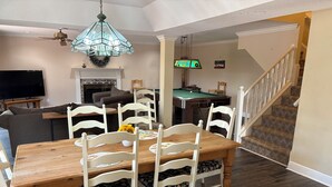A dining area with a wooden table and white chairs, a pool table, a television, and a staircase.