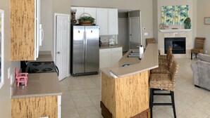 Una cocina moderna con una isla central, refrigerador de acero inoxidable y una chimenea en la sala de estar.