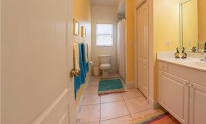 Een kleine badkamer met toilet, wastafel en douche. Handdoeken hangen aan de muur en er ligt een kleurrijk vloerkleed.