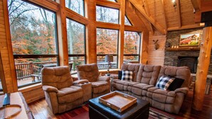 A cozy cabin interior with large windows, a fireplace, and comfortable seating. - Stream Front Log Home near 7 Springs, 4 BR (Rockwood)