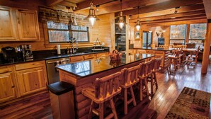 A spacious kitchen with wooden cabinets, a large island with bar stools, and a stone fireplace. - Stream Front Log Home near 7 Springs, 4 BR (Rockwood)