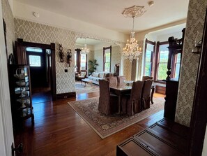 A dining area with a wooden table, chairs, and a chandelier. There is a sofa and a window in the background. - Gorgeous Historic Victorian Duplex, Quick Walk to Wharf, Beach & Boardwalk (Santa Cruz)