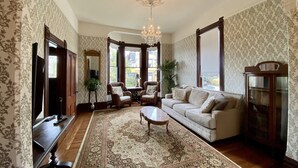 Un salón tradicional con un gran tapiz estampado, un sofá, sillones, una mesa de centro de madera y una araña.