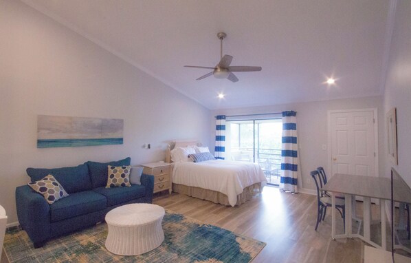 Un dormitorio con una cama, un sofá azul, un sillón blanco, una mesa de comedor y un ventilador de techo.
