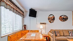 Ein gemütlicher Raum mit einem Holzesstisch, Bänken, einer Couch und zwei an der Wand befestigten Fernsehern.