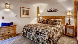 Ein Schlafzimmer mit einem Holzkopfende, einer gesteppten Bettdecke, zwei Nachttischlampen, einer Holzkommode und einem gerahmten Bild an der Wand.