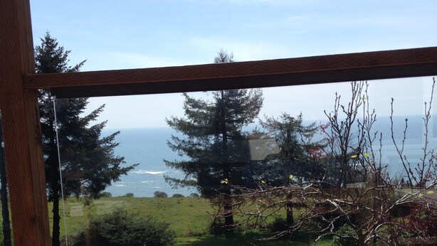 Una terraza de madera con vistas al océano y un paisaje verde con árboles.