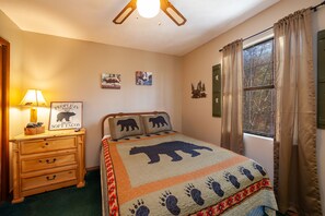 Un dormitorio con cama, mesita de noche, lámpara y ventana con cortinas.