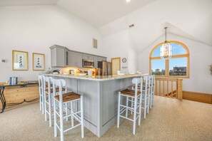 A kitchen with a central island, bar stools, and a large window. - Soundfront Home w/ Hot Tub, Windsports Access, Community Tennis and Pickleball (Rodanthe)