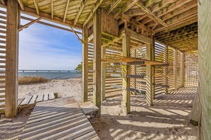 Une structure en bois située sur la plage, dotée d’une terrasse en bois et offrant une vue sur la plage et la mer.