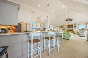 A spacious kitchen with a bar area, a dining space with a sofa, and a view of the outside. - Soundfront Home w/ Hot Tub, Windsports Access, Community Tennis and Pickleball (Rodanthe)