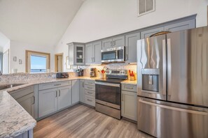 A modern kitchen with grey cabinets, stainless steel appliances, and a large window.