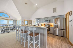 A spacious kitchen with modern appliances, a bar area with stools, and a view of the sea through large windows.