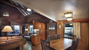 A cozy cabin interior with a wooden dining table, chairs, a sofa, and a bar area.
