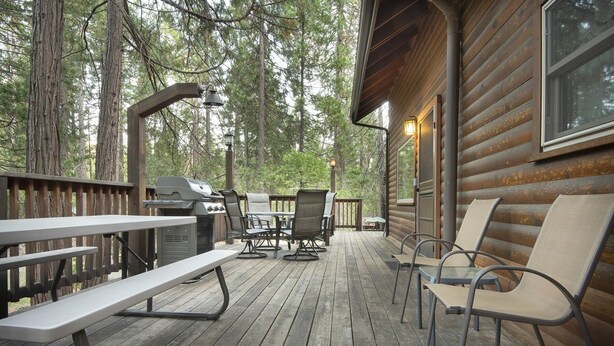 A wooden deck with picnic tables and chairs, a grill, and a cabin with large windows.