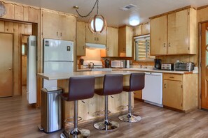 A compact kitchen with wooden cabinets, a central island with bar stools, a refrigerator, a microwave, a coffee maker, and a dishwasher.
