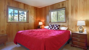 Un dormitorio con un revestimiento de madera, una cama con colcha roja, dos lámparas de noche y una mesita de noche con lámpara.