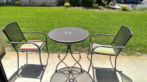 A patio with two chairs and a table, set on a concrete surface with a grassy lawn in the background.