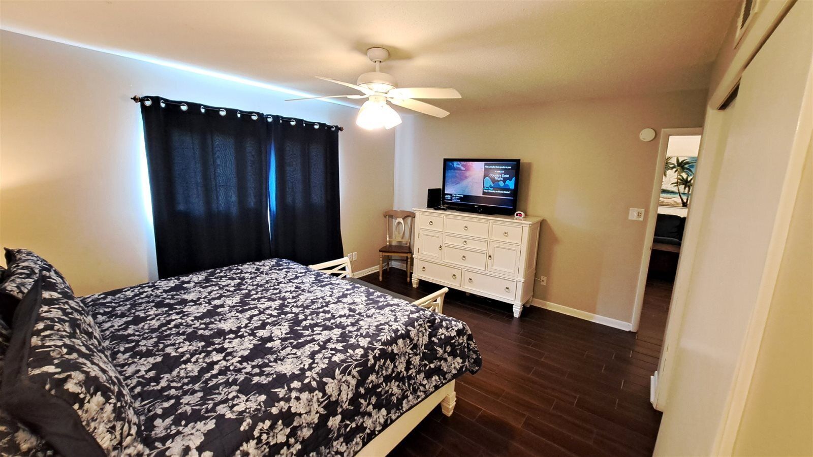A bedroom with a bed, a dresser, a television, and a ceiling fan.