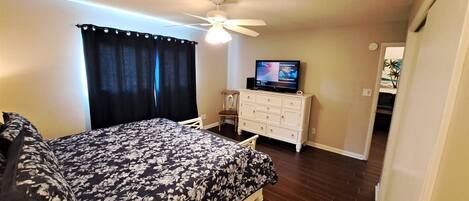 A bedroom with a bed, a dresser, a television, and a ceiling fan.