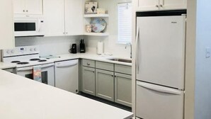 Cuina moderna amb armaris blancs, una illa central i electrodomèstics integrats.