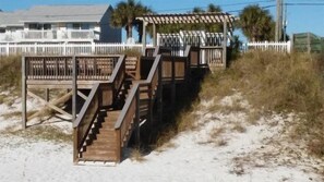 Wooden boardwalks leading to beach houses with white fences and palm trees.