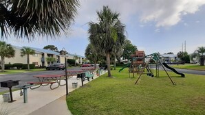 Un parc amb taules de pícnic, un parc infantil i un edifici al fons.
