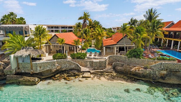 A resort with a clear turquoise pool, stone bridges, and palm trees. - Oceanfront with private beach - 4 bedrooms, 4 bathrooms (Kralendijk)