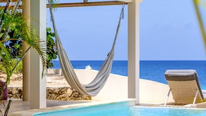 A pool area with a hammock, a lounge chair, and a view of the ocean. - Oceanfront with private beach - 4 bedrooms, 4 bathrooms (Kralendijk)