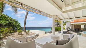 A covered outdoor seating area with a view of the ocean, white furniture, and a hammock. - Oceanfront with private beach - 4 bedrooms, 4 bathrooms (Kralendijk)