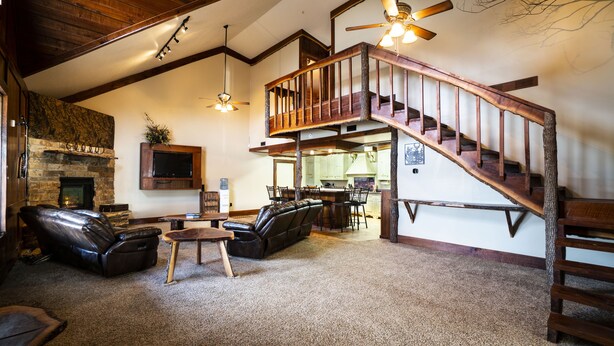 A spacious living area with a fireplace, leather sofas, a wooden staircase, and a dining area. - PEACEFUL PLAYGROUND.  130 acres of fun.  RV hookups available too. (Udall)