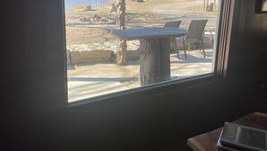 A room with a large window overlooking a patio area with a table and chairs. - PEACEFUL PLAYGROUND.  130 acres of fun.  RV hookups available too. (Udall)