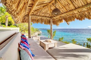 A beachside lounge with a thatched roof, wooden furniture, and a view of the ocean. - Villa Shores 32, a secluded oceanfront villa with sea access (Kralendijk)