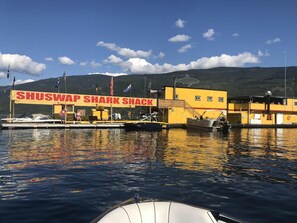 Un edificio amarillo con un letrero que dice "SHUSWAP SHARK SHACK" y un muelle con barcos.