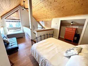 A bedroom with a wooden ceiling, a bed with white bedding, a dresser, and a window with blinds.