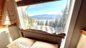 Un dormitorio con cama, ventana con vistas a un bosque y montañas, y cabecero de madera.