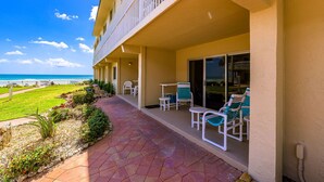 Hotel con balcón que da a una playa, mobiliario exterior y un jardín bien cuidado.