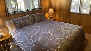 Dormitorio de cabaña de madera con cama, mesitas de noche y ventanas.