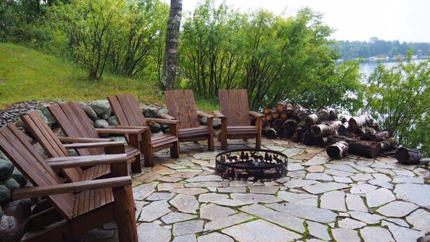 Um pátio de pedra com cadeiras Adirondack e uma lareira.