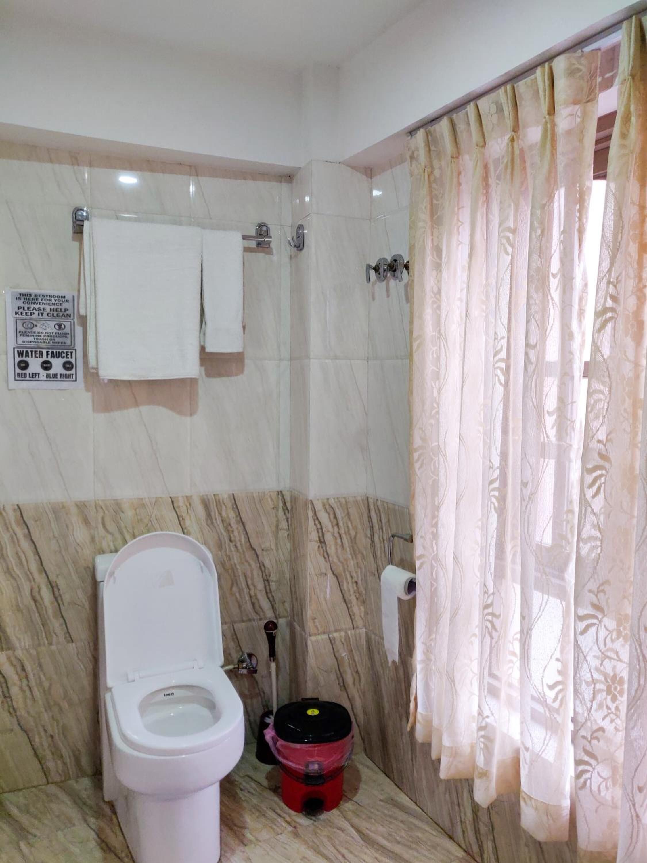 A bathroom with a toilet, a water faucet, a trash bin, and a shower curtain.