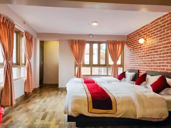 Habitación de hotel con dos camas, una pared de ladrillo y ventanas amplias con cortinas.